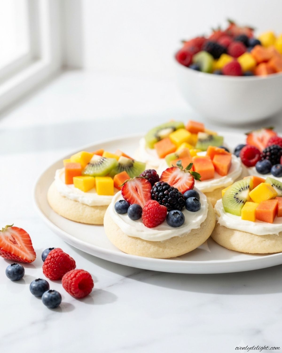 Easy Mini Fruit Pizzas decorated with strawberries, blueberries, kiwi, and creamy frosting on buttery cookies.